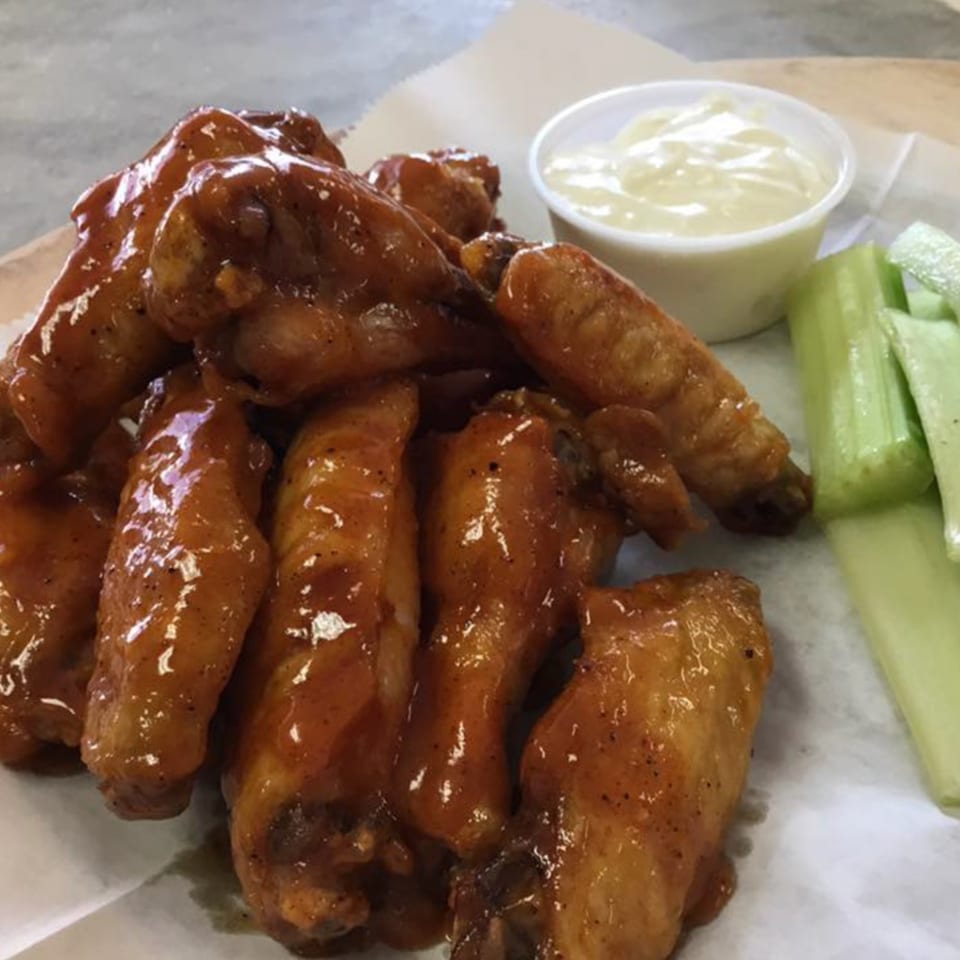 Plate of Vito's Bistro's glazed chicken wings with a side of celery sticks and dipping sauce.