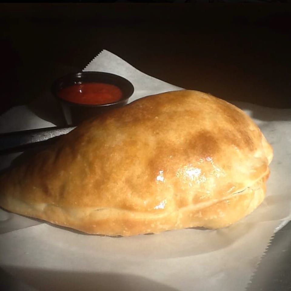 Golden-brown calzone on parchment paper with a side of red marinara sauce at Vito's Bistro.