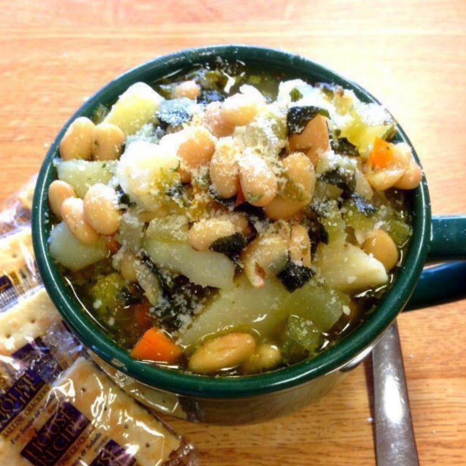 Hearty minestrone soup with beans, vegetables, and grated cheese in a green mug, with crackers.