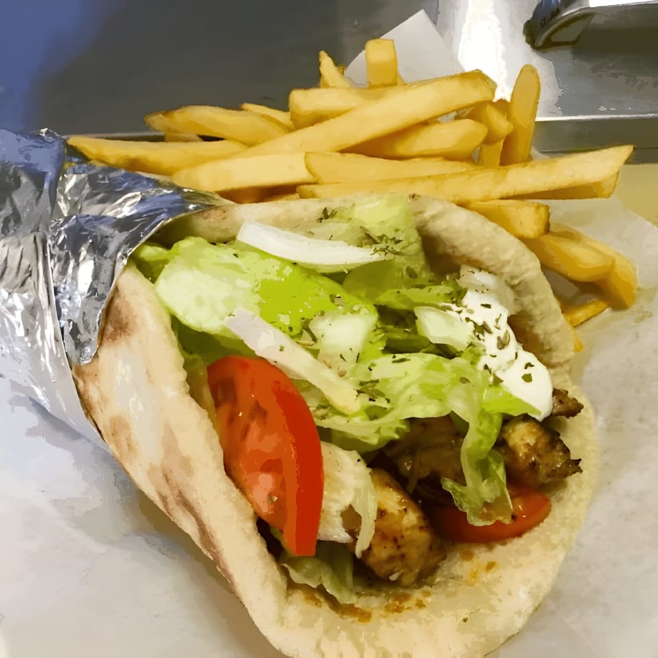 A chicken gyro wrapped in foil with lettuce, tomato, and sauce, served with a side of french fries.