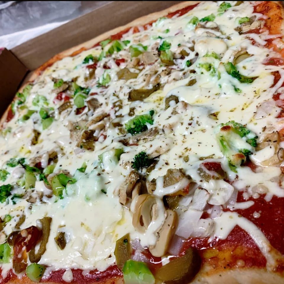 Close-up of a Vito's Bistro pizza with melted cheese, broccoli, mushrooms, and peppers in a box.