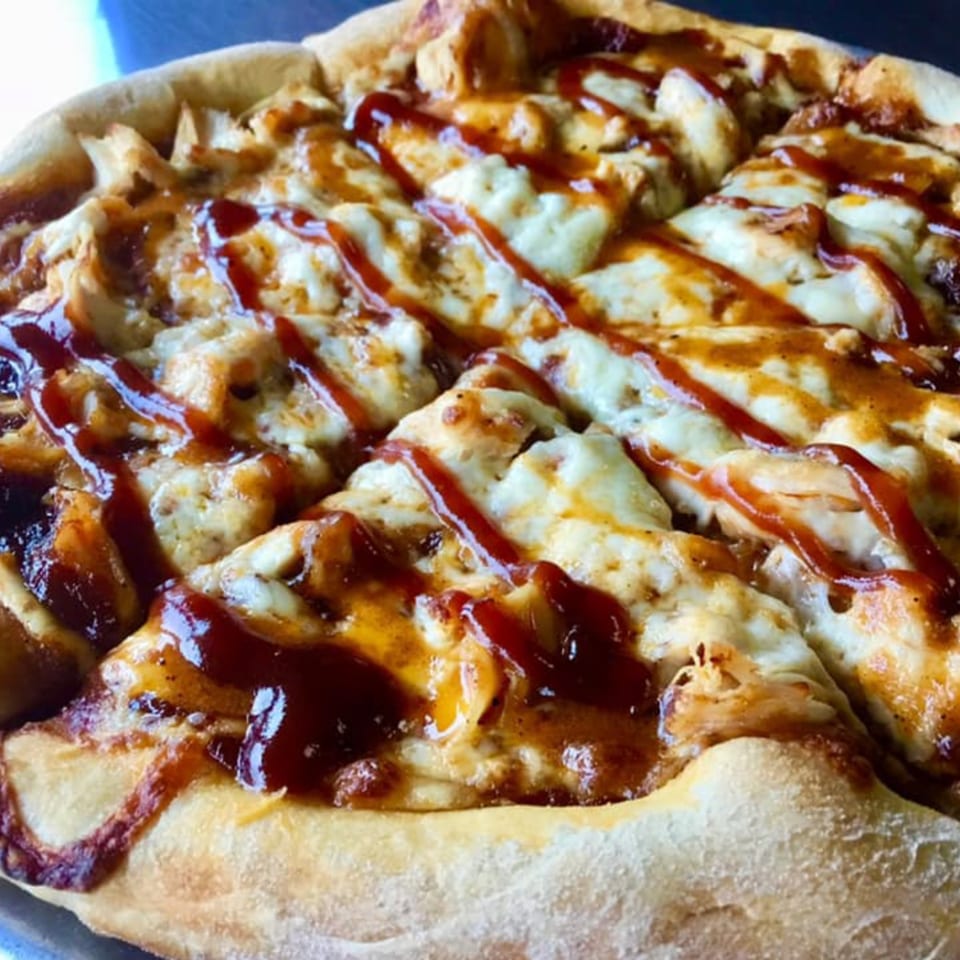 Close-up of a sliced BBQ chicken pizza from Vito's Bistro, drizzled with sauce.