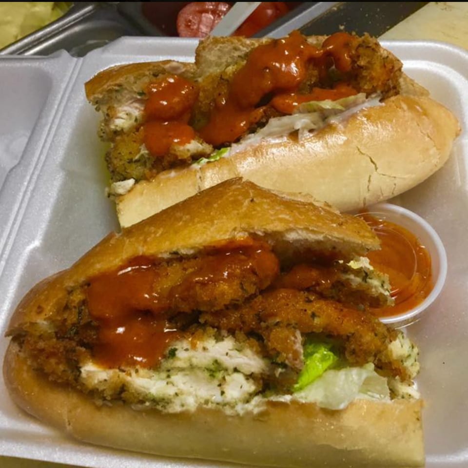 Two crispy chicken sandwiches with red sauce, lettuce, and a side of sauce in a styrofoam container.