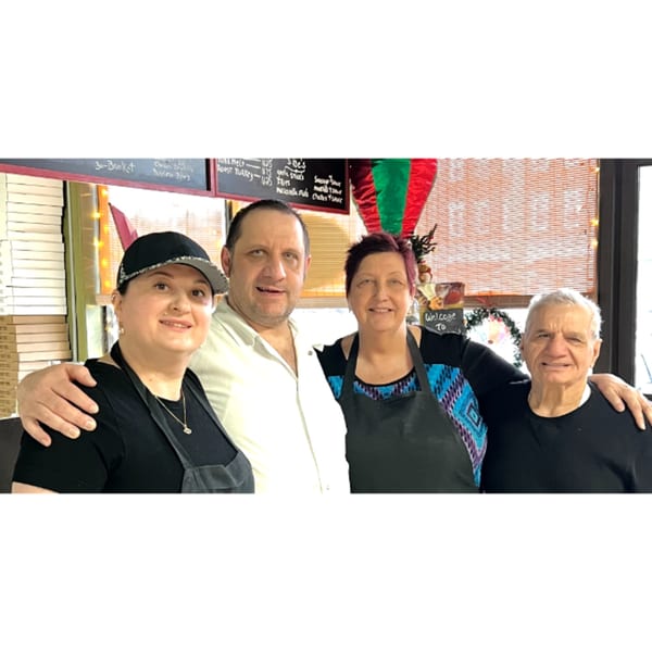 Four smiling people, two men and two women, stand together in a restaurant setting.