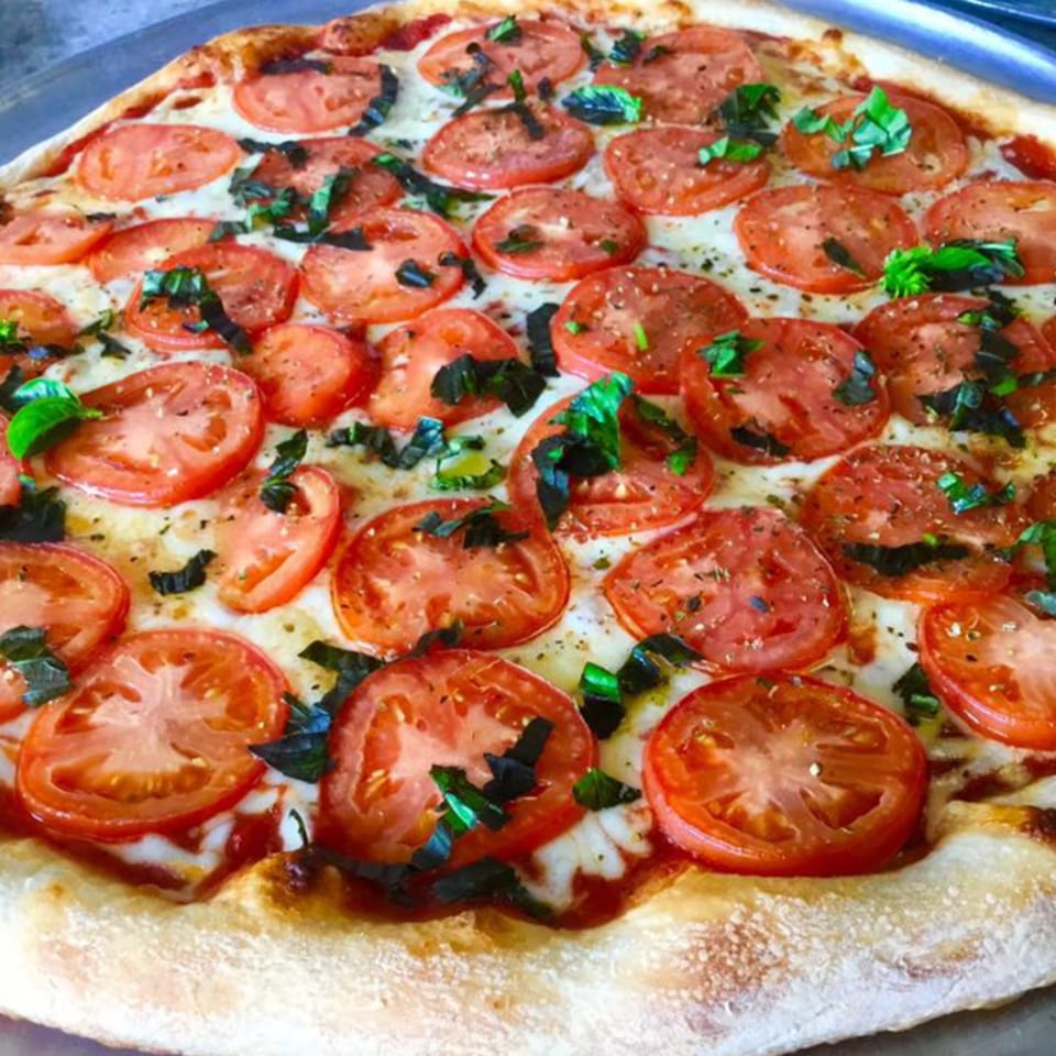 Close-up of a Vito's Bistro Margherita pizza with sliced tomatoes, mozzarella, and fresh basil.