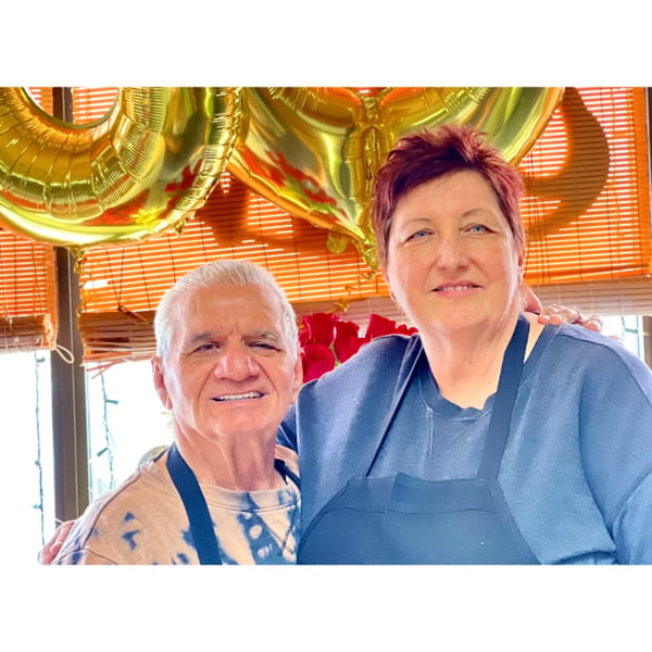 Vito's Bistro owners, a man and woman, smiling with golden balloons and red roses in the background.